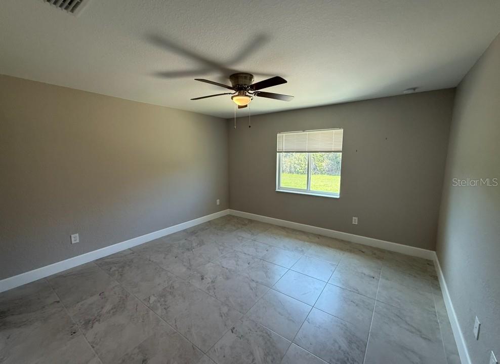 An empty bedroom features light gray walls, large marble-look floor tiles, and a ceiling fan — 113 BOUNDARY BOULEVARD UNIT 2, ROTONDA WEST, FL