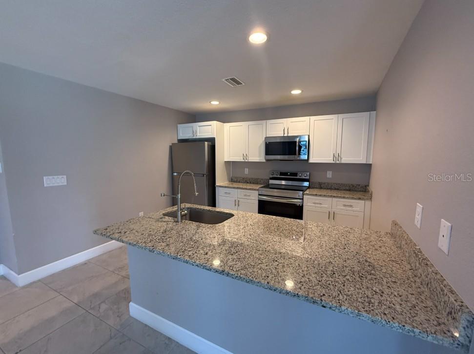 A kitchen features white cabinets, granite countertops, stainless steel appliances, and a breakfast bar — 113 BOUNDARY BOULEVARD UNIT 2, ROTONDA WEST, FL