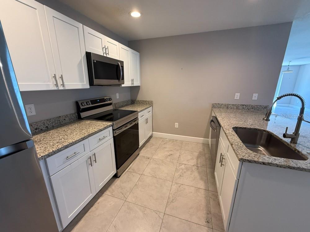 A kitchen with white cabinets, granite countertops, stainless steel appliances, and light-colored tile flooring — 113 BOUNDARY BOULEVARD UNIT 2, ROTONDA WEST, FL