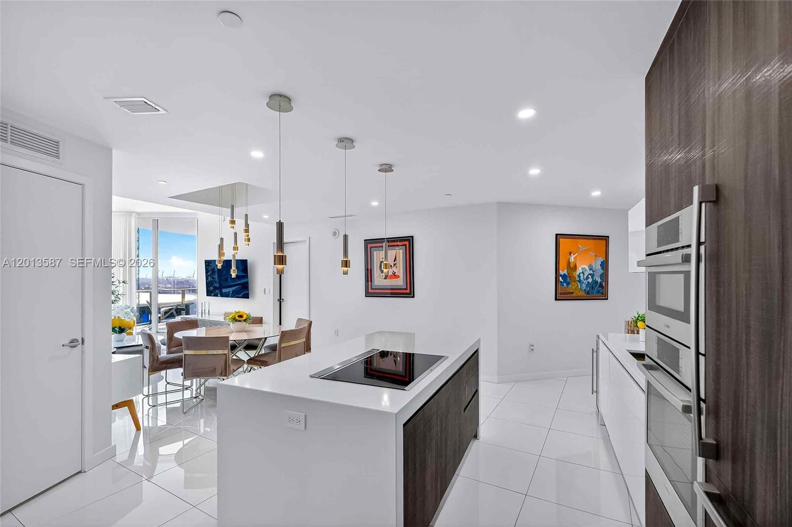 A modern kitchen with a white island and dark wood cabinetry opens to a dining area — 851 NE 1st Ave # 1603, Miami FL 33132, MIAMI, FL