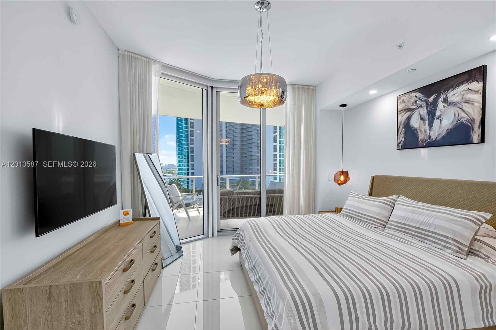 A modern bedroom features a striped bed, a wall-mounted television, and a balcony with city views — 851 NE 1st Ave # 1603, Miami FL 33132, MIAMI, FL