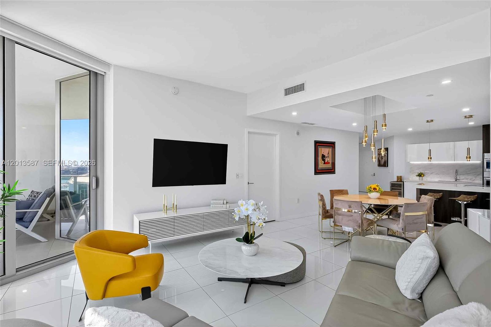 A modern living and dining area features white tile floors, a yellow chair, and balcony — 851 NE 1st Ave # 1603, Miami FL 33132, MIAMI, FL