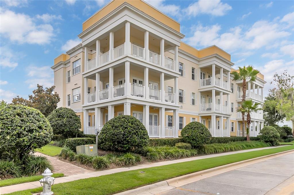 A multi-story apartment building with white balconies and yellow exterior walls sits near a road — 7474 EXCITEMENT DR UNIT 203, REUNION, FL