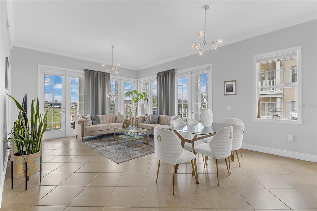 A bright open-concept living and dining area features tile flooring, modern lighting, and glass doors — 7474 EXCITEMENT DR UNIT 203, REUNION, FL