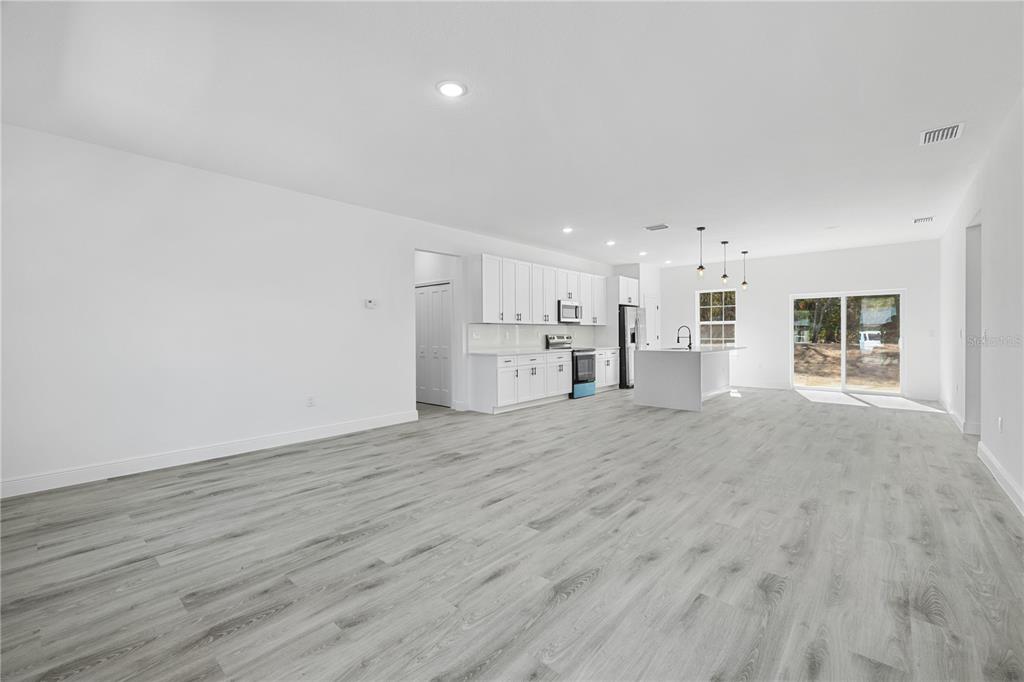 A bright, open-concept kitchen and living area featuring white cabinetry, an island, and wood-look flooring — 7674 N VOYAGER DRIVE, CITRUS SPRINGS, FL
