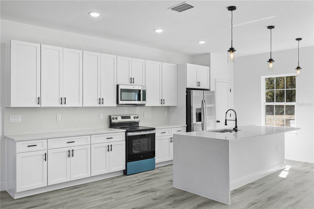 A modern kitchen features white cabinets, quartz countertops, stainless steel appliances, and a central island — 7674 N VOYAGER DRIVE, CITRUS SPRINGS, FL