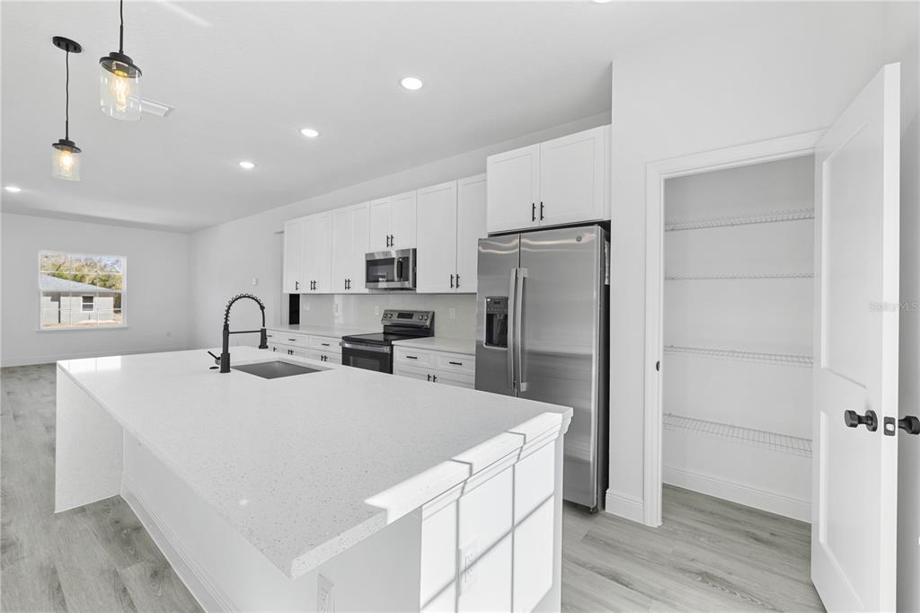 A modern kitchen features a large white island, stainless steel appliances, and a walk-in pantry — 7674 N VOYAGER DRIVE, CITRUS SPRINGS, FL