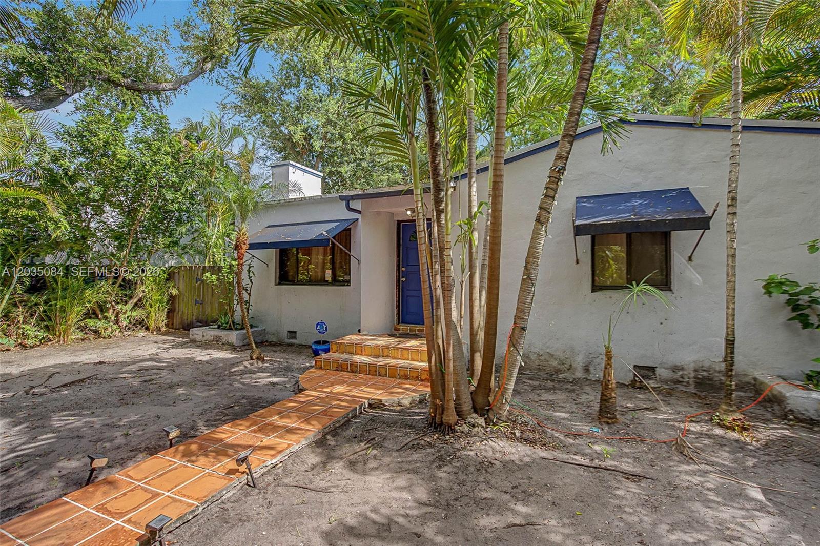 A white house with a tiled walkway, blue awnings, and palm trees in the front yard — 583 NW 47th St, Miami FL 33127, MIAMI, FL