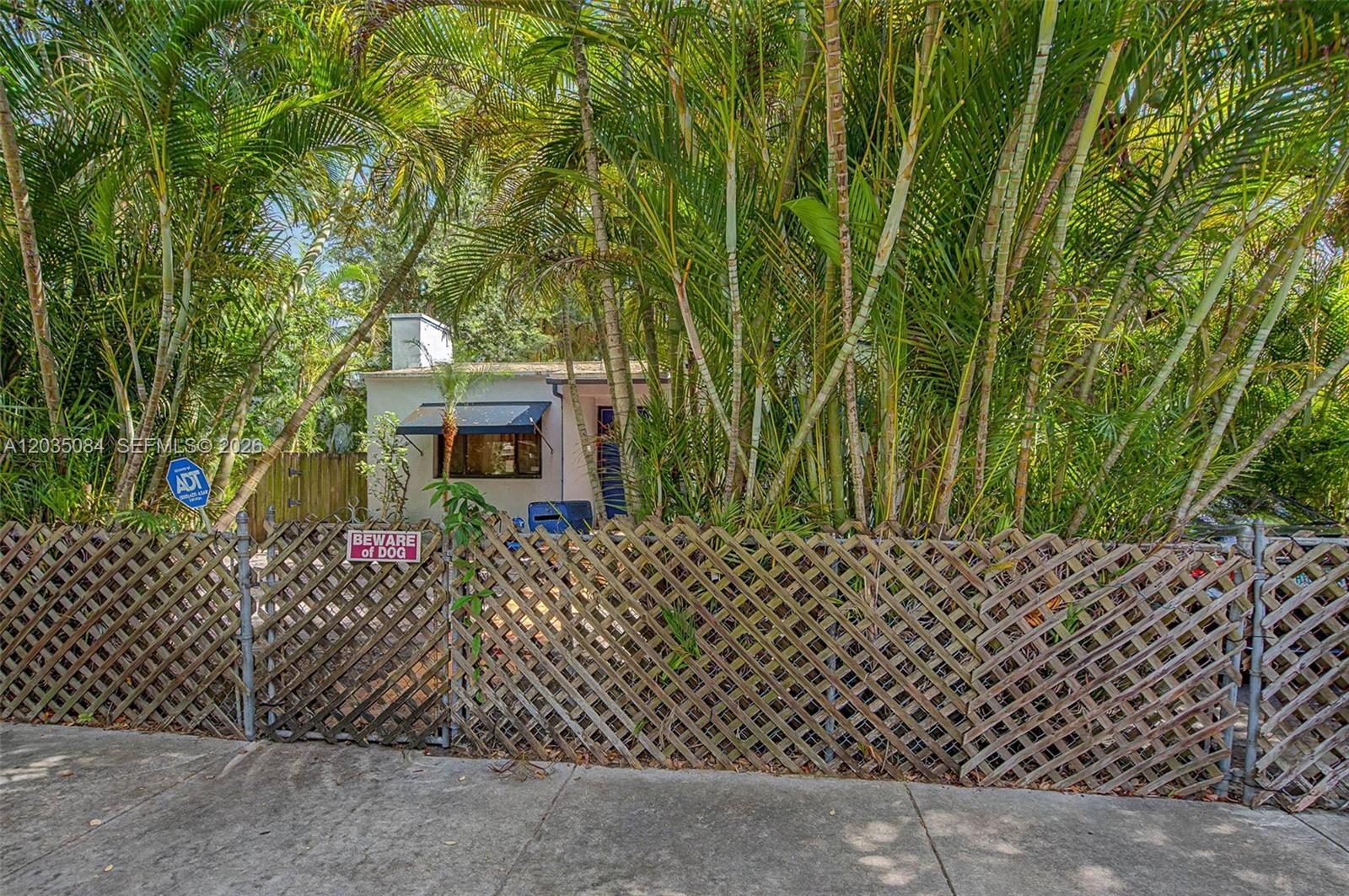 A small house is partially obscured by dense palm trees behind a wooden lattice fence — 583 NW 47th St, Miami FL 33127, MIAMI, FL