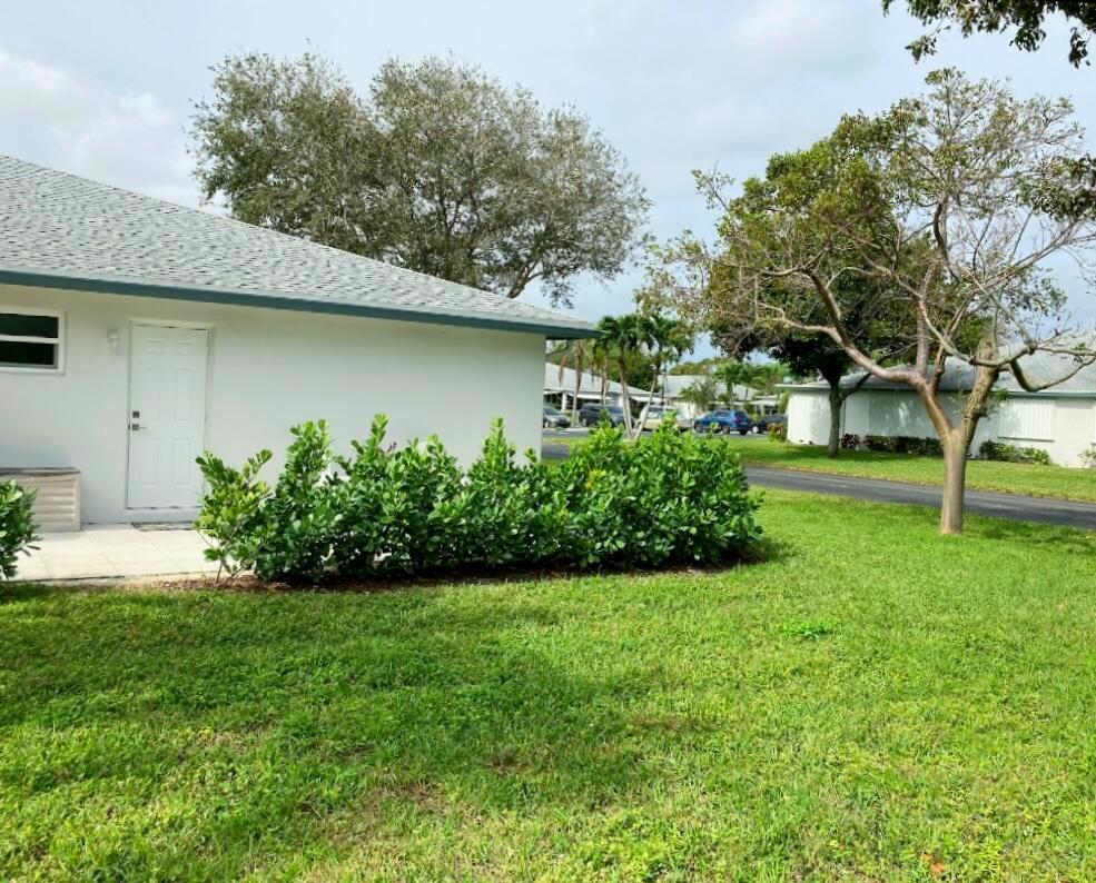 A white exterior wall with a door and a green hedge in a grassy yard — 1155 S Drive Circle # A, Delray Beach FL 33445, DELRAY BEACH, FL