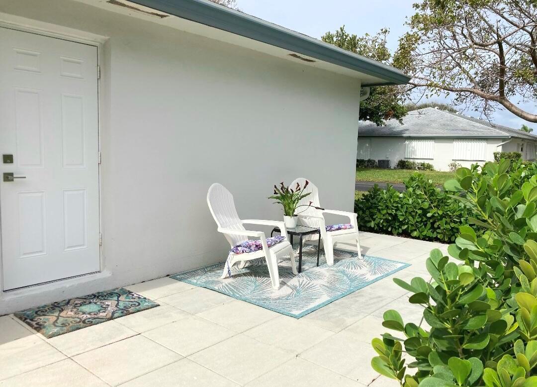 A white exterior wall with a door and a patio featuring two chairs and rug — 1155 S Drive Circle # A, Delray Beach FL 33445, DELRAY BEACH, FL