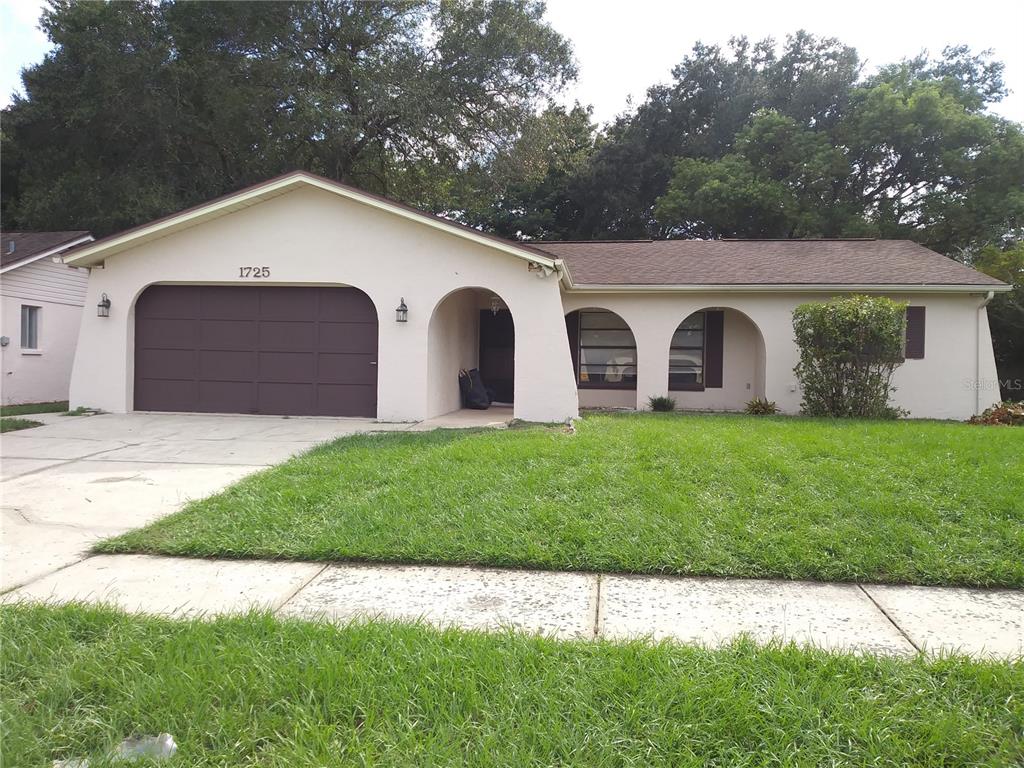 A single-story house with a brown garage door, arched entryway, and a front lawn — 1725 TUMBLEWEED DRIVE, HOLIDAY, FL