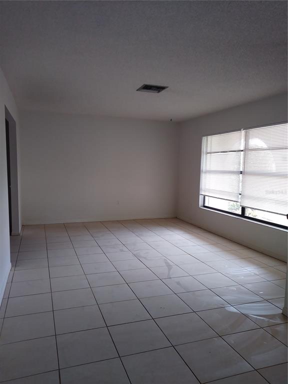 An empty room features white walls, light-colored tile flooring, and a large window with blinds — 1725 TUMBLEWEED DRIVE, HOLIDAY, FL