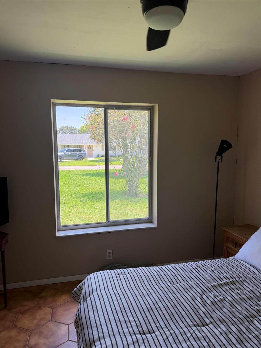 A bedroom features a striped bed, a window overlooking a yard, and tile flooring — 3079 Indian Trail, Lake Worth FL 33462, LAKE WORTH, FL