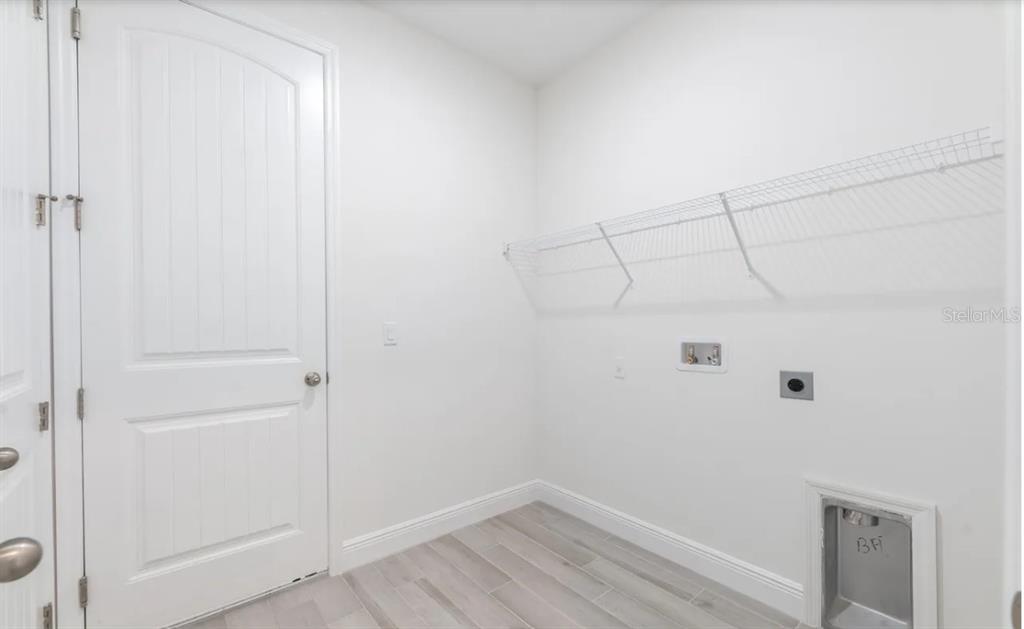 A laundry room with white walls, light wood-look tile flooring, and a wire storage shelf — 335 FRANZING ST SW, PALM BAY, FL