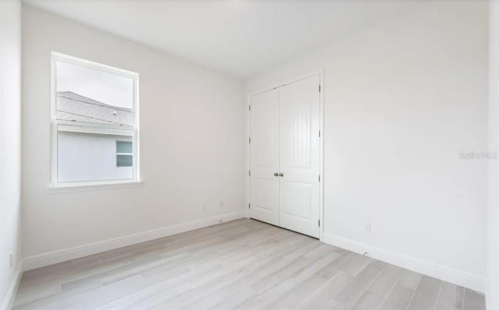 An empty bedroom features white walls, light-colored wood-look flooring, a window, and a closet — 335 FRANZING ST SW, PALM BAY, FL
