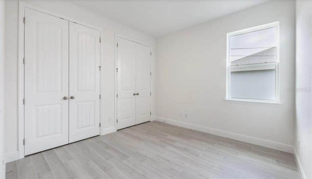 A bedroom with white walls, light wood-look tile flooring, and two sets of closet doors — 335 FRANZING ST SW, PALM BAY, FL