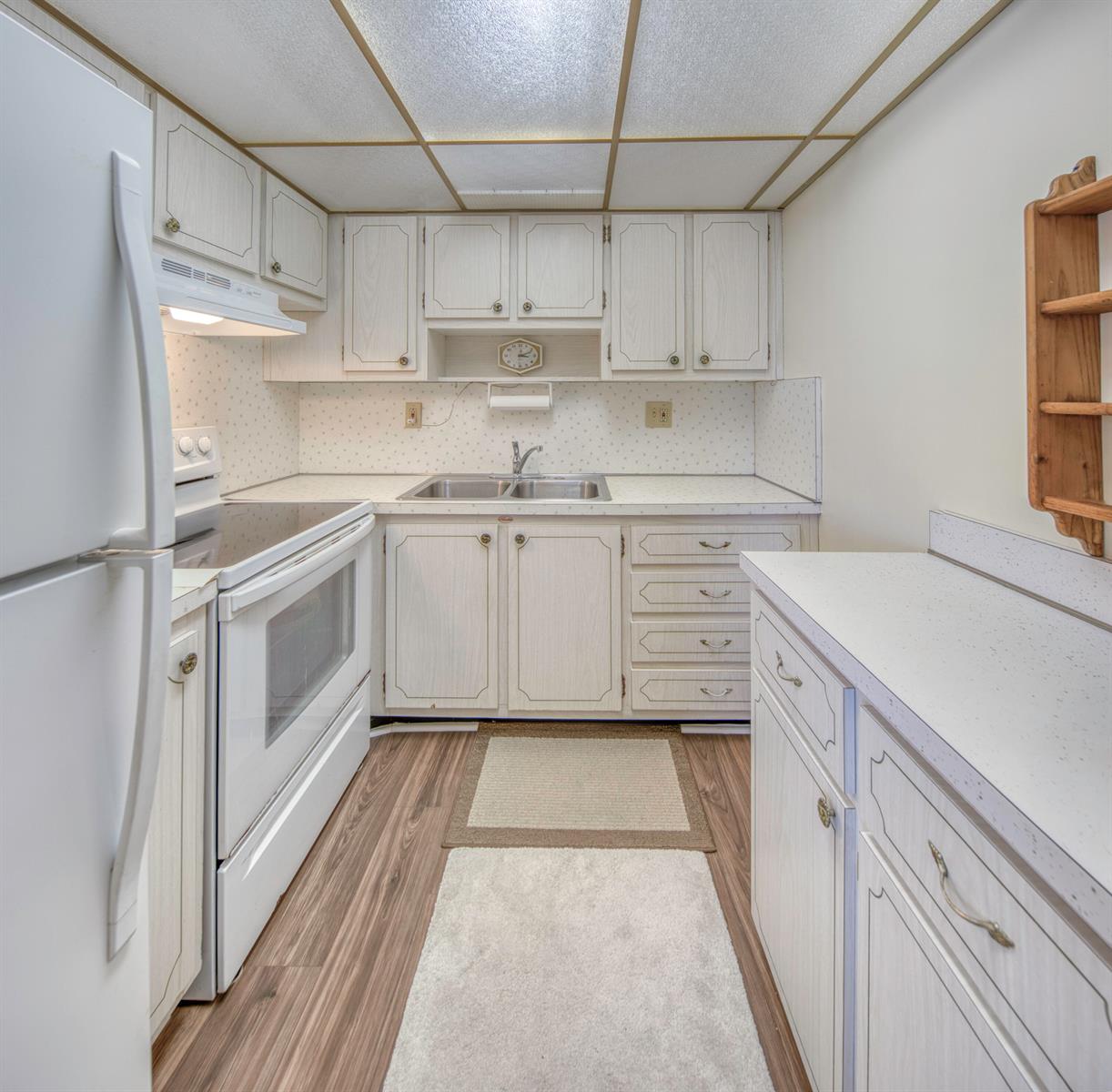 A galley kitchen features white cabinets, laminate countertops, wood-look flooring, and a drop ceiling — 1980 Sunset Avenue # 19, FL 33461, FL