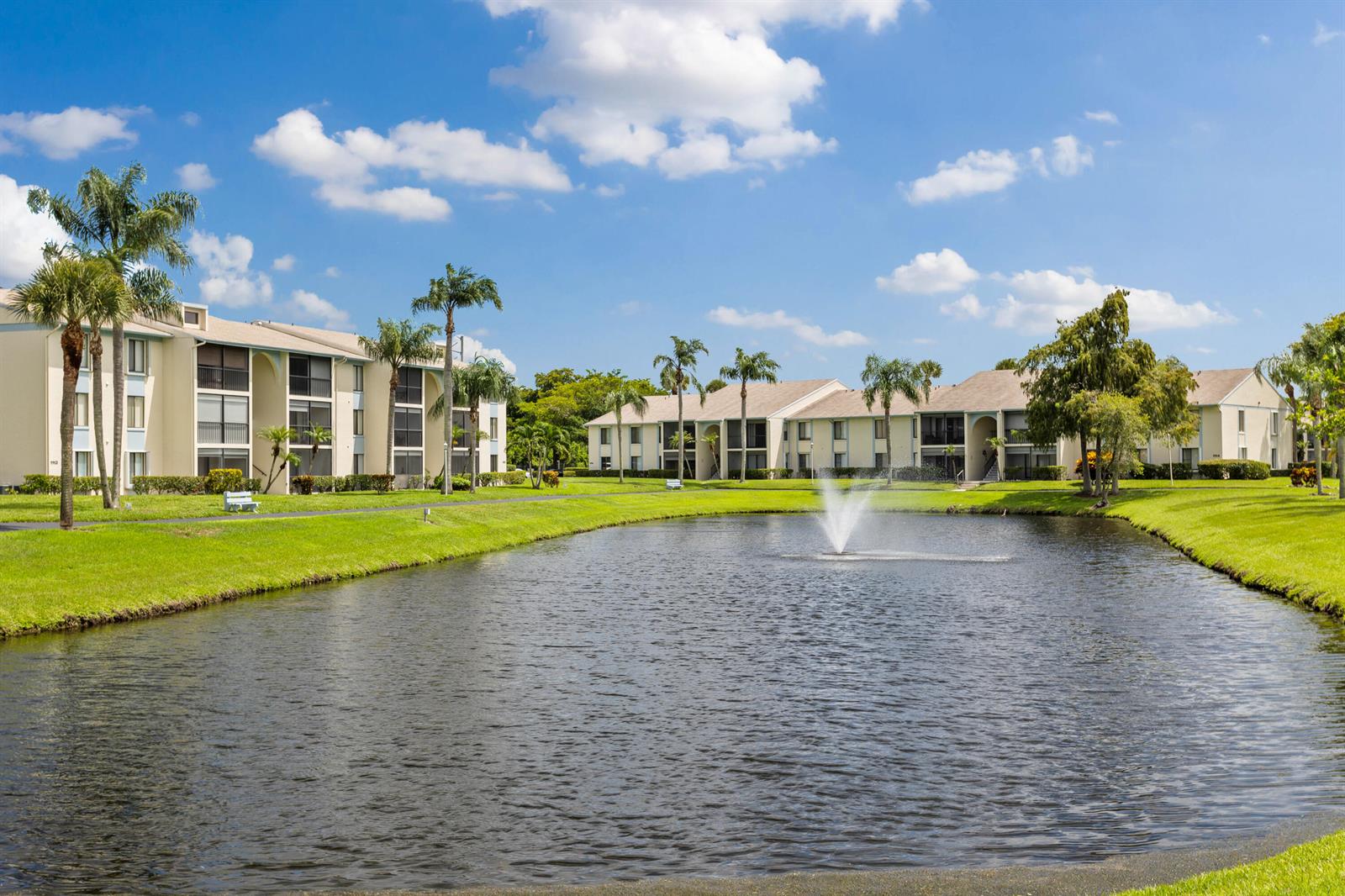A pond with a fountain sits in front of two multi-story apartment buildings with palms — 1102 Green Pine Boulevard # H1, West Palm Beach FL 33409, WEST PALM BEACH, FL