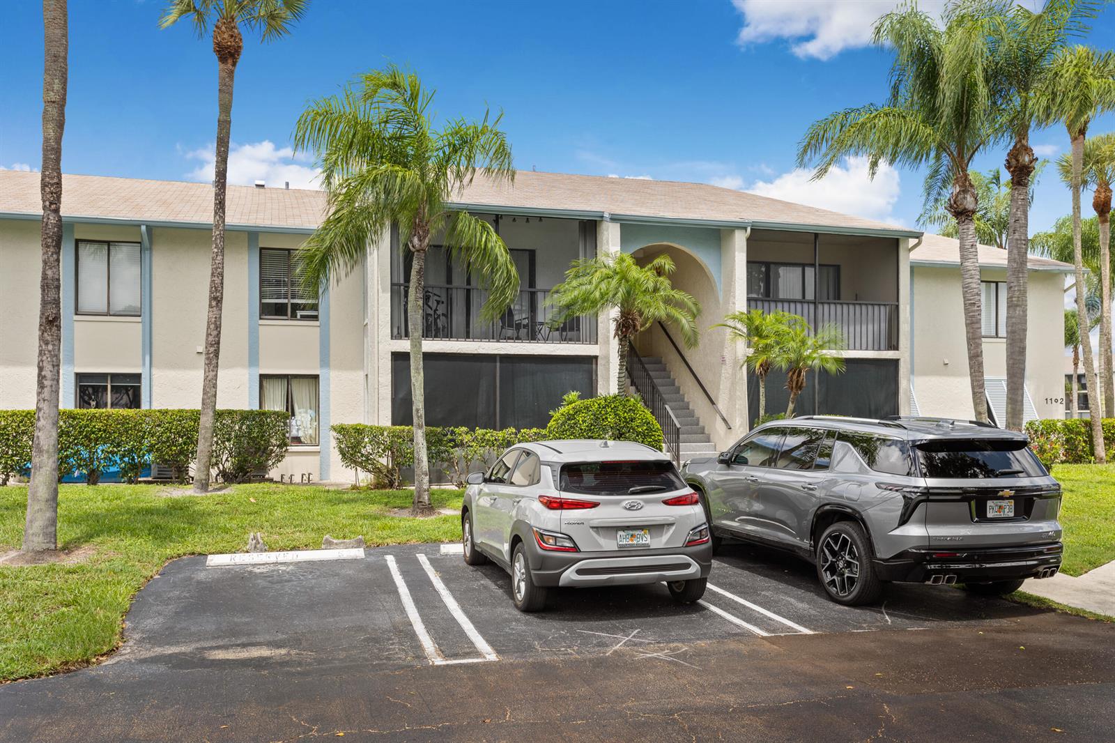 A two-story apartment building with screened balconies and two parked cars in the foreground — 1102 Green Pine Boulevard # H1, West Palm Beach FL 33409, WEST PALM BEACH, FL