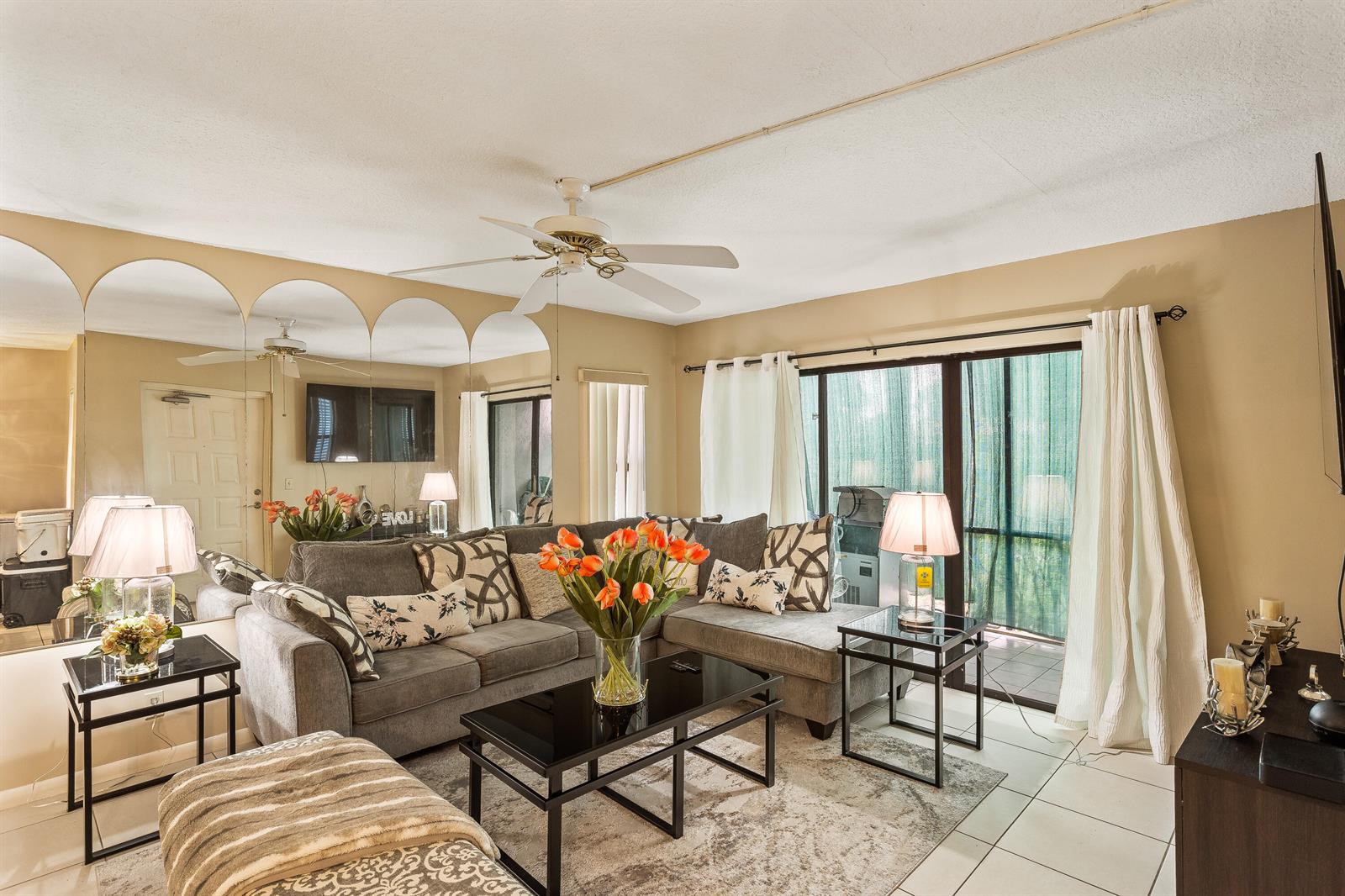 A living room features a gray sectional sofa, a black coffee table, and a mirrored wall — 1102 Green Pine Boulevard # H1, West Palm Beach FL 33409, WEST PALM BEACH, FL