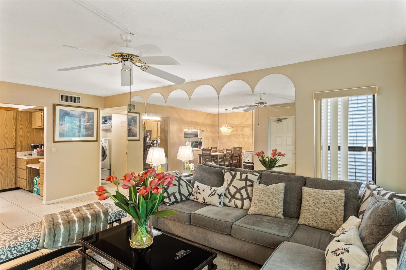 A living room features a grey sectional sofa, a black coffee table, and arched wall mirrors — 1102 Green Pine Boulevard # H1, West Palm Beach FL 33409, WEST PALM BEACH, FL