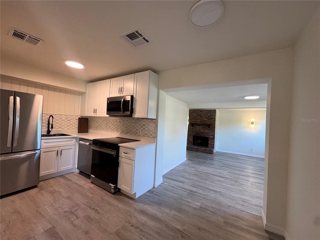 A modern kitchen with white cabinets and stainless steel appliances opens into a living room — 7224 VALIANT COURT, ORLANDO, FL