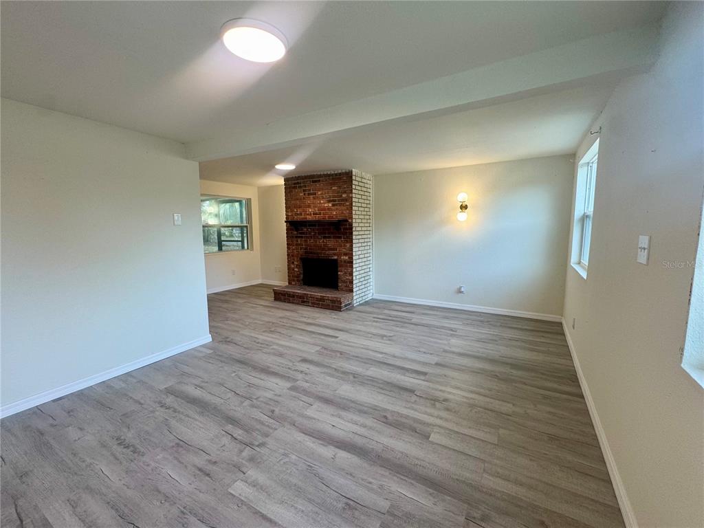 A living room features light wood-look flooring, white walls, and a central brick fireplace — 7224 VALIANT COURT, ORLANDO, FL