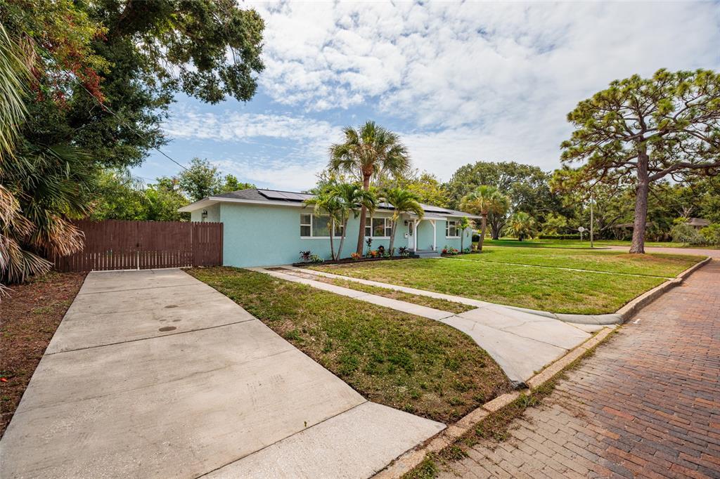 A light blue single-story house features a concrete driveway, a wooden fence, and palm trees — 801 61ST STREET N, ST PETERSBURG, FL