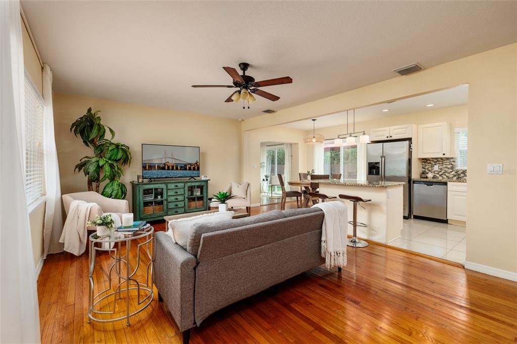 An open-concept living room and kitchen feature hardwood floors, a gray sofa, and stainless appliances — 801 61ST STREET N, ST PETERSBURG, FL