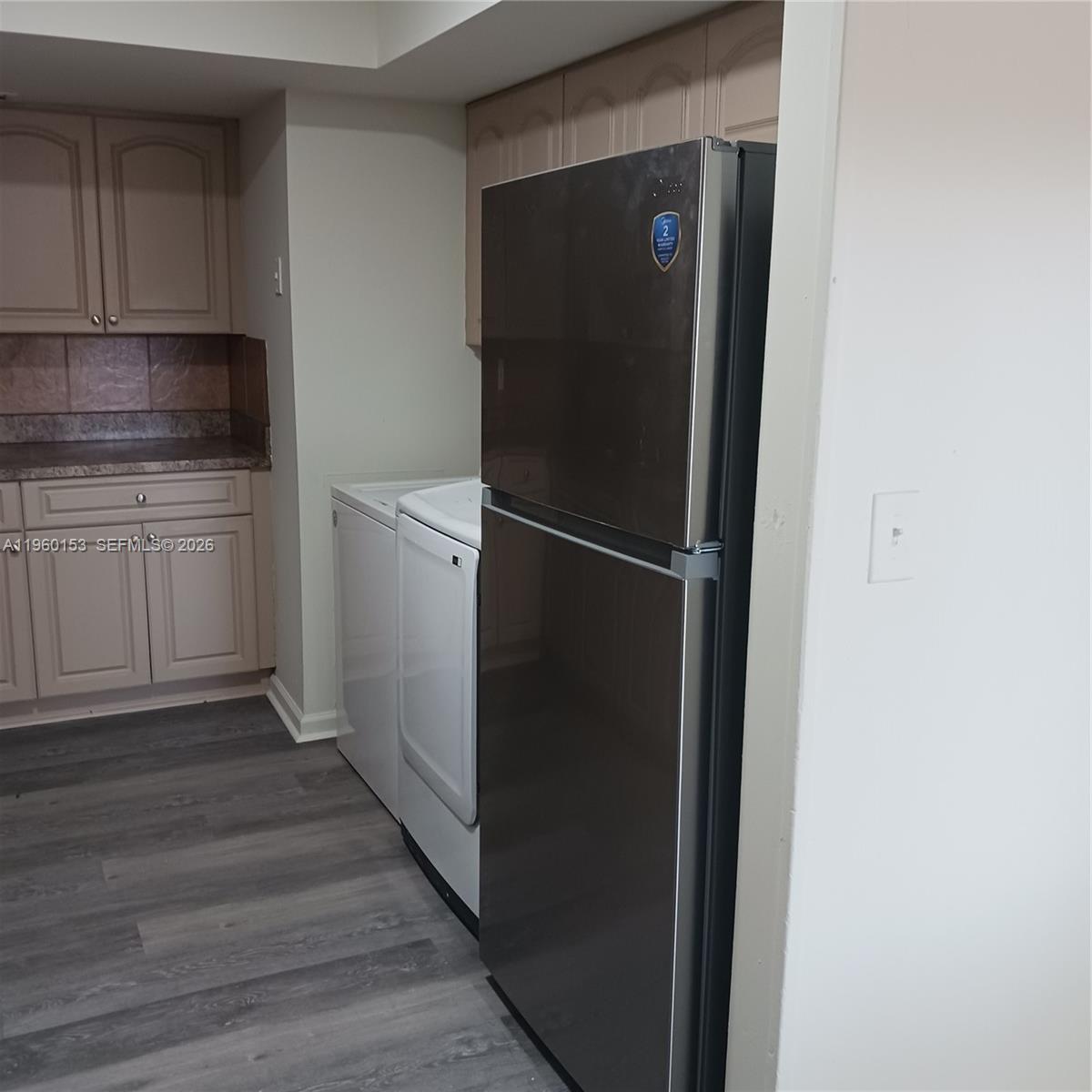 A kitchen area features light-colored cabinets, a stainless steel refrigerator, and white laundry appliances — 2107 NW 59th Ter, Lauderhill FL 33313, LAUDERHILL, FL
