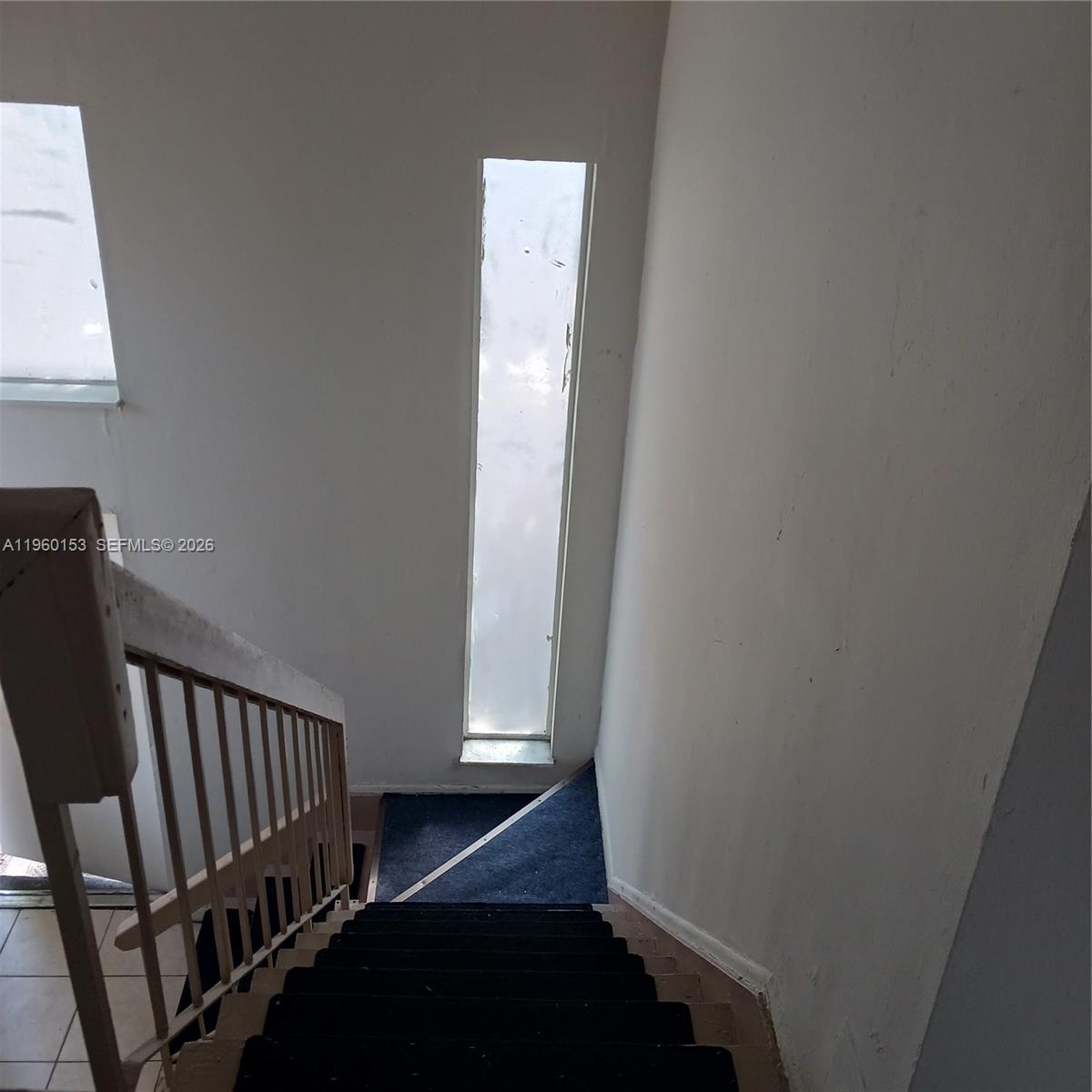 A staircase with dark carpeted steps leads down to a landing with a tall window — 2107 NW 59th Ter, Lauderhill FL 33313, LAUDERHILL, FL