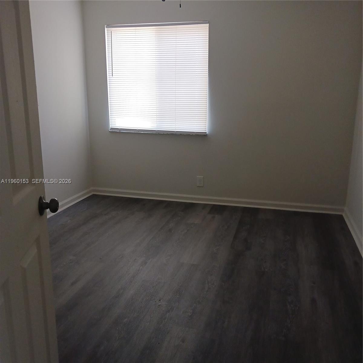 An empty bedroom features grey wood-look flooring, white walls, and a window with blinds — 2107 NW 59th Ter, Lauderhill FL 33313, LAUDERHILL, FL