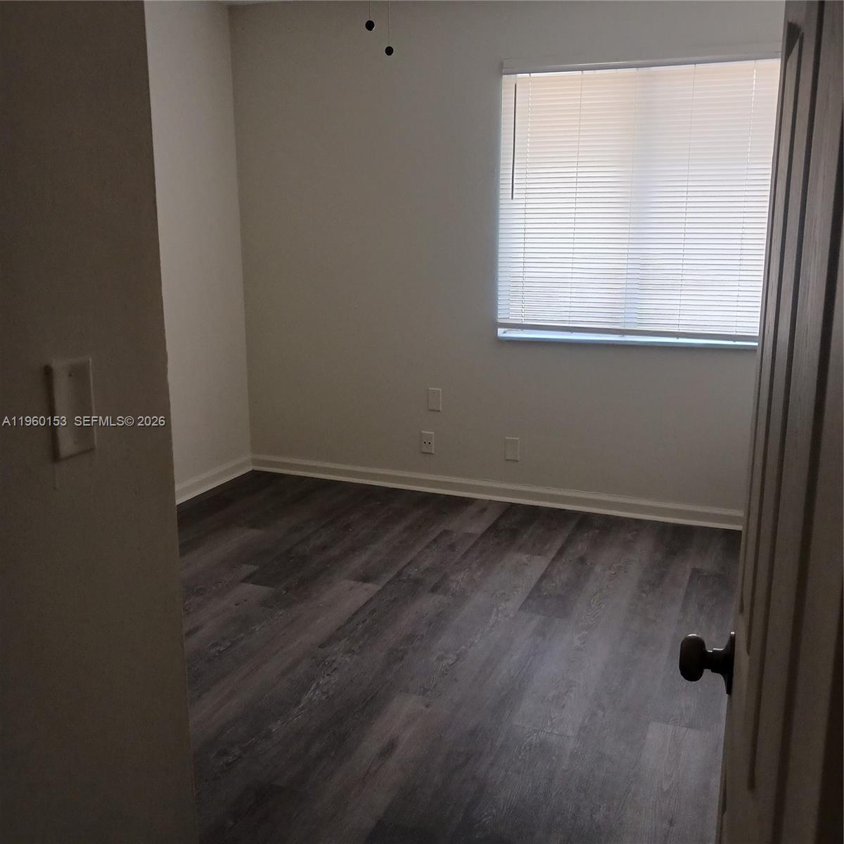 An empty bedroom features grey wood-look flooring, light-colored walls, and a window with blinds — 2107 NW 59th Ter, Lauderhill FL 33313, LAUDERHILL, FL