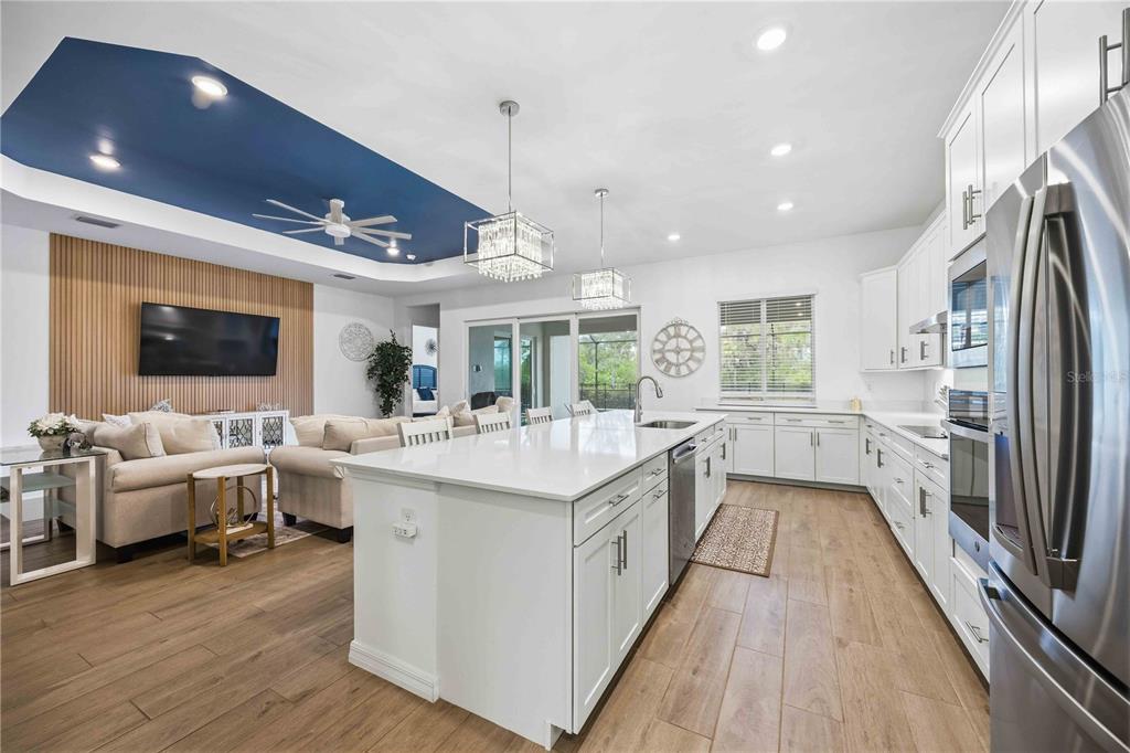 An open-concept kitchen and living area features white cabinetry, a large island, and wood flooring — 17365 JADESTONE COURT, VENICE, FL