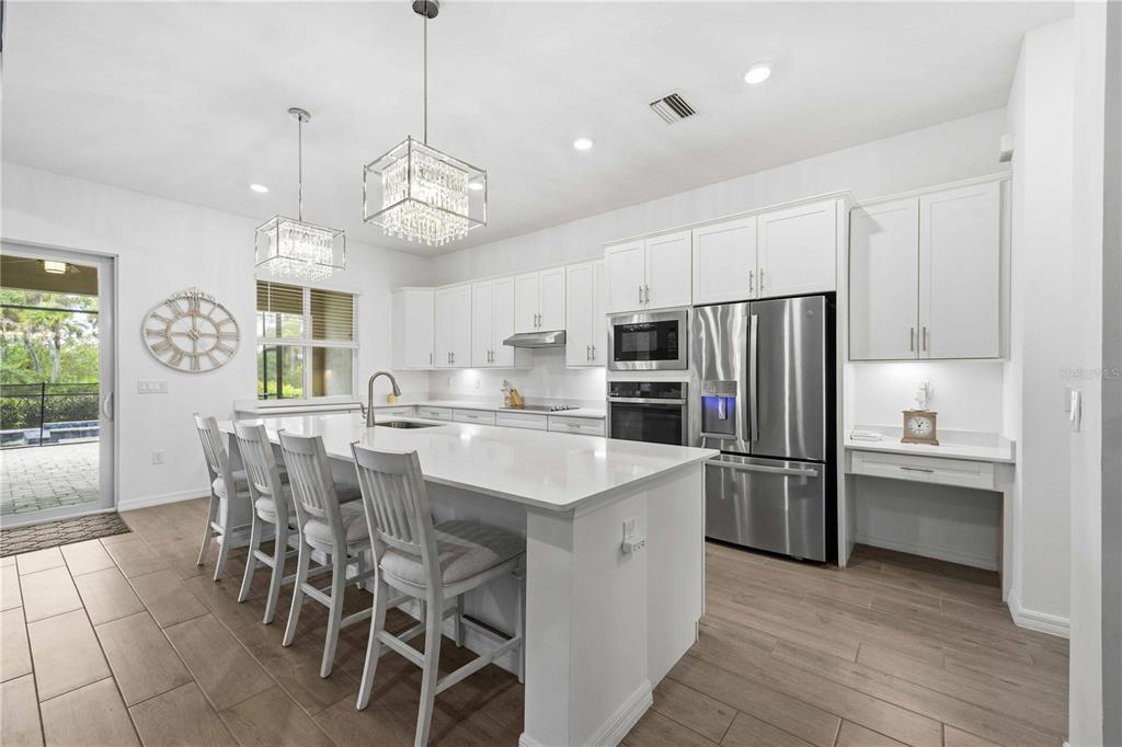 A modern white kitchen features a large island, stainless steel appliances, and tile flooring — 17365 JADESTONE COURT, VENICE, FL