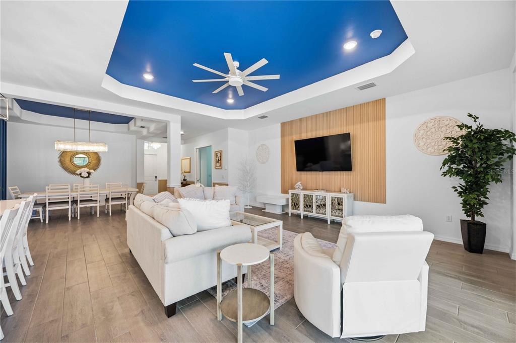 A living room features a blue tray ceiling, wood-slat wall paneling, and white furniture — 17365 JADESTONE COURT, VENICE, FL