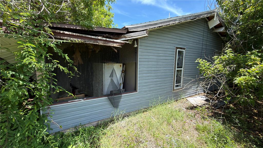 An exterior view of a weathered, gray-sided house with a damaged porch and overgrown vegetation — 5110 HONEY LANE, GRANT, FL