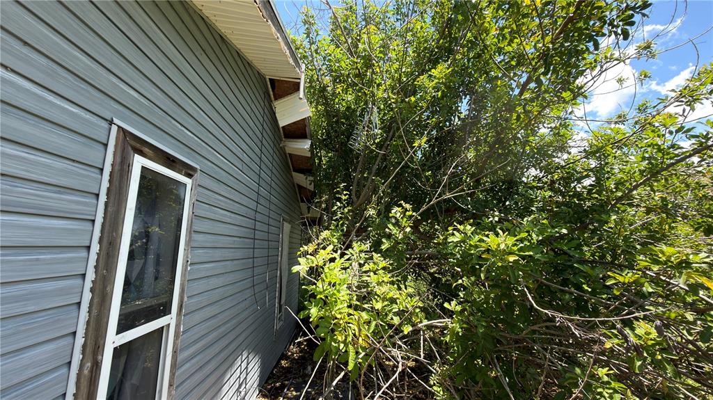 A side view of a house with gray vinyl siding and overgrown trees nearby — 5110 HONEY LANE, GRANT, FL