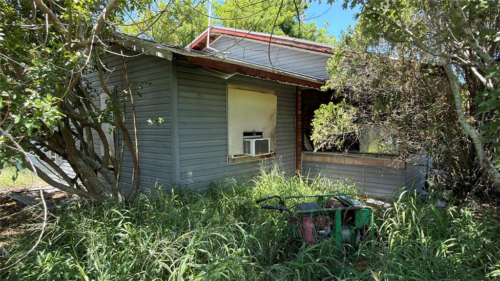 An overgrown yard surrounds a weathered, gray-sided house with a window air conditioning unit — 5110 HONEY LANE, GRANT, FL