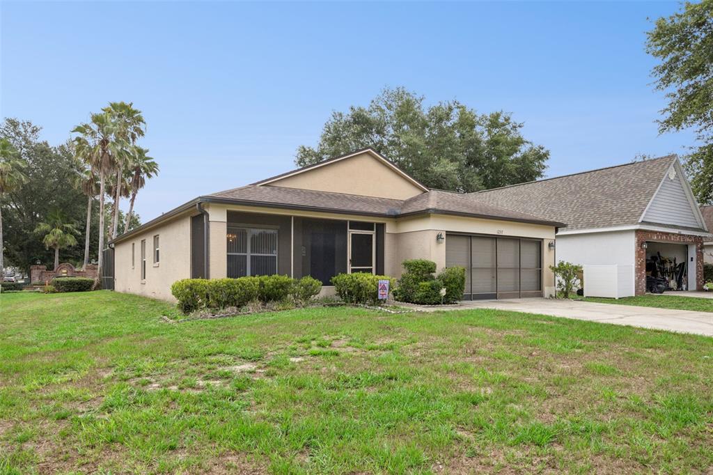 A single-story house with a screened front porch and a garage sits on a lawn — 1237 WOODFLOWER WAY, CLERMONT, FL
