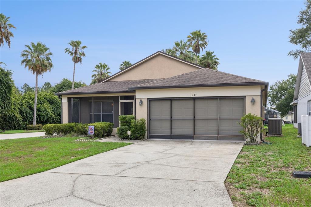 A single-story house with a beige exterior, a screened-in garage, and a concrete driveway — 1237 WOODFLOWER WAY, CLERMONT, FL
