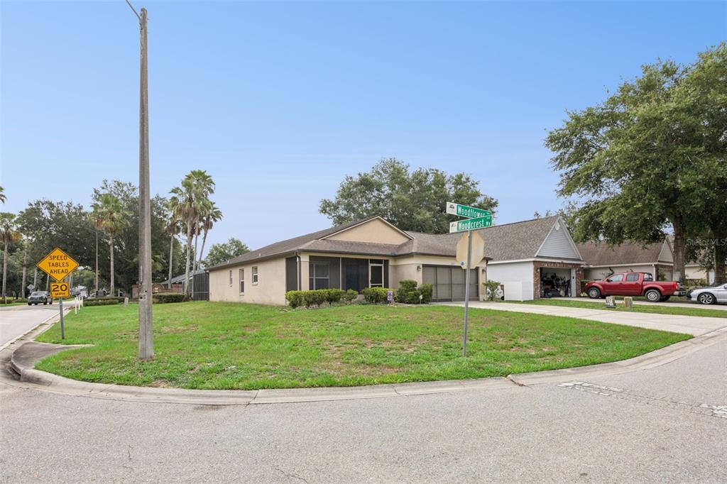 A single-story house with a tan exterior and a screened porch sits on a corner lot — 1237 WOODFLOWER WAY, CLERMONT, FL