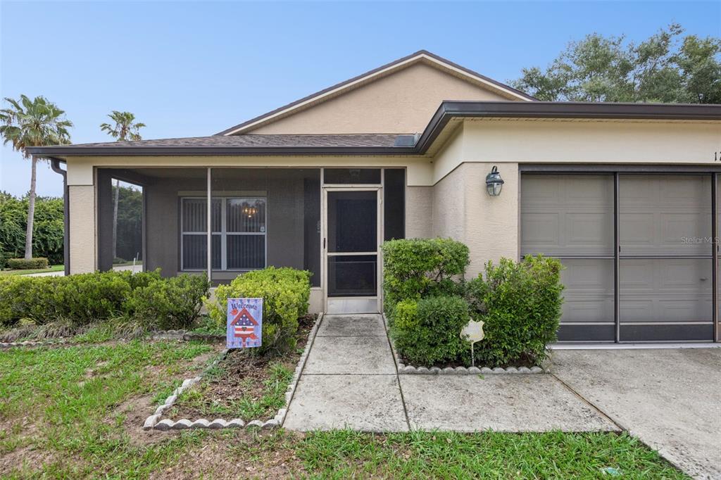 The exterior of a single-story house features a screened-in porch, a concrete walkway, and a garage — 1237 WOODFLOWER WAY, CLERMONT, FL