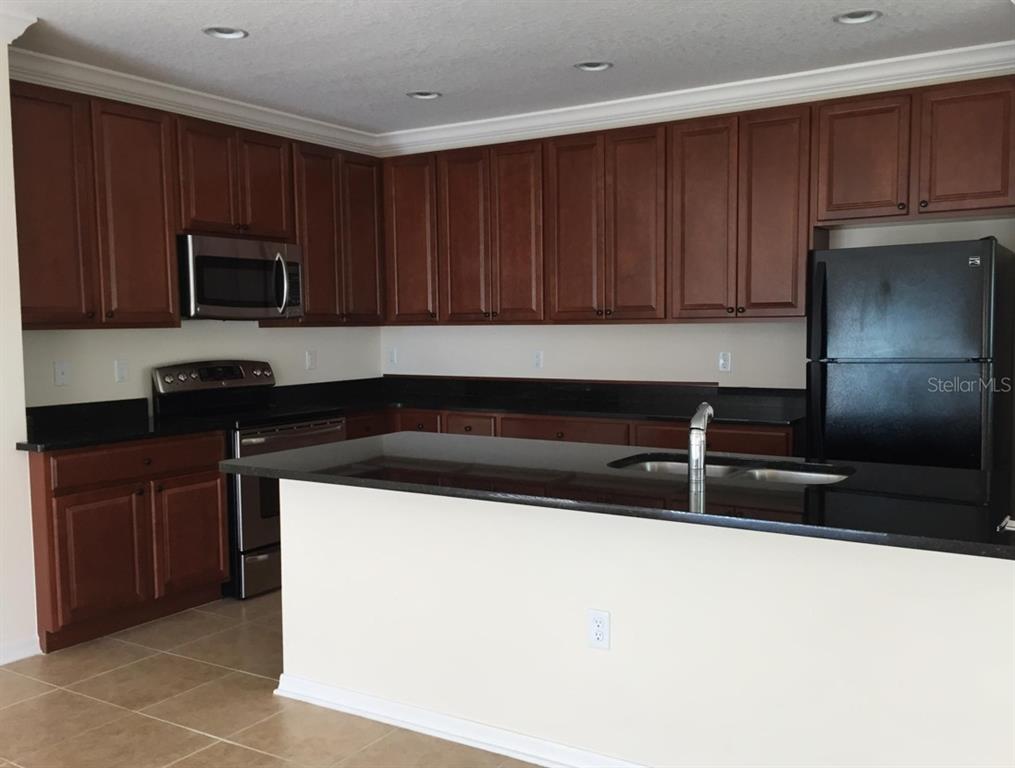 A kitchen features dark wood cabinets, black countertops, stainless steel appliances, and a central island — 3938 SUNSET COVE DRIVE, PORT ORANGE, FL