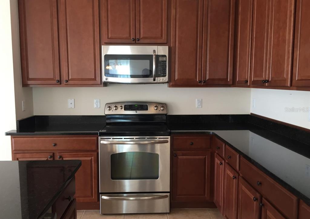 A kitchen features dark wood cabinets, black countertops, and stainless steel appliances — 3938 SUNSET COVE DRIVE, PORT ORANGE, FL