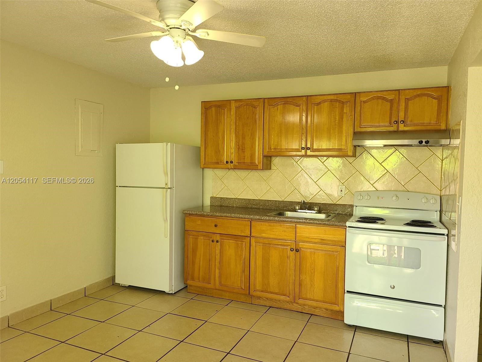 A kitchen features light wood cabinets, white appliances, a tiled backsplash, and beige floor tiles — 2117 Liberty St, Hollywood FL 33020, HOLLYWOOD, FL