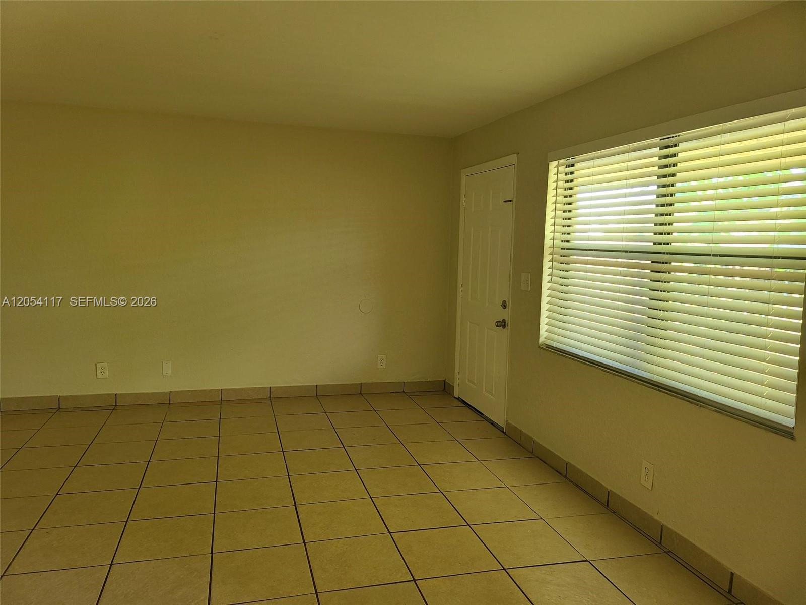 An empty room features beige walls, light-colored tile flooring, and a window with white blinds — 2117 Liberty St, Hollywood FL 33020, HOLLYWOOD, FL