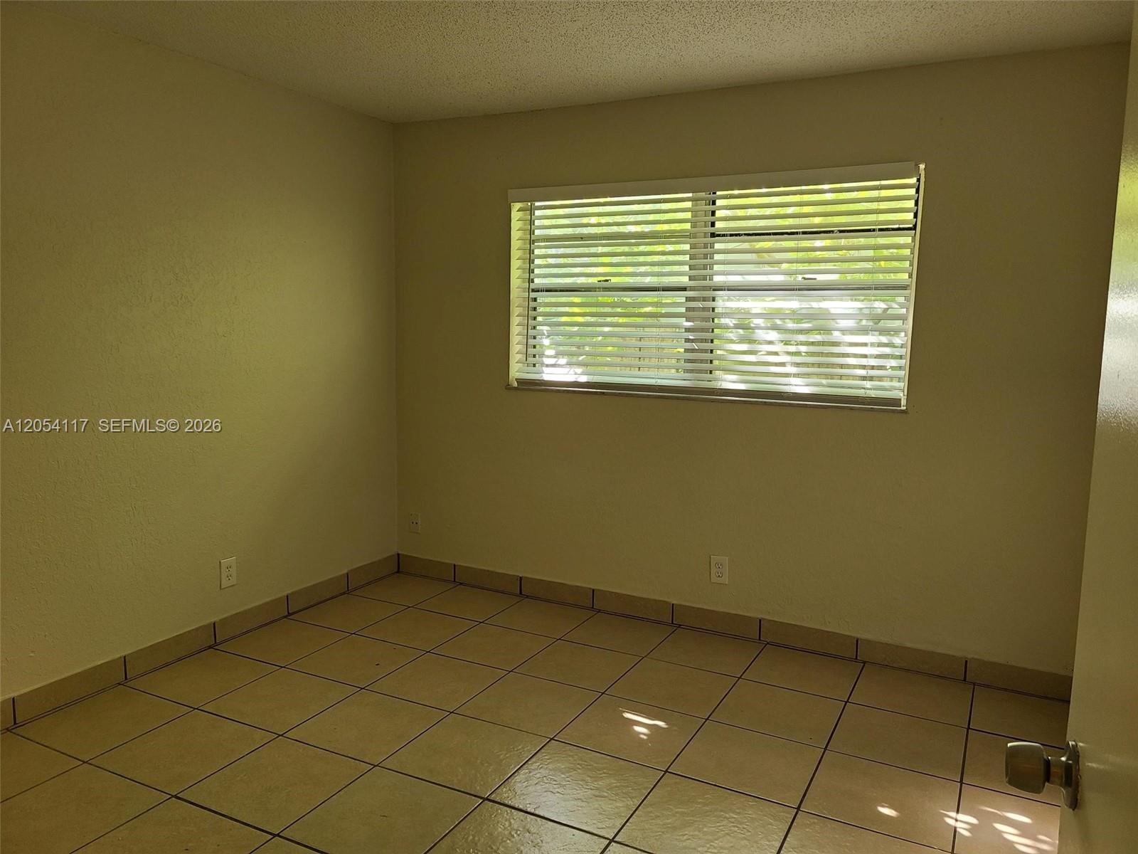 An empty room features beige walls, tiled flooring, and a window with horizontal blinds — 2117 Liberty St, Hollywood FL 33020, HOLLYWOOD, FL