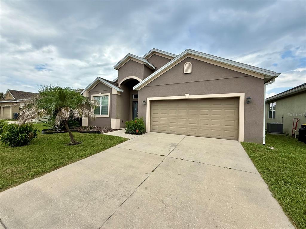 A single-story house with a tan stucco exterior, a two-car garage, and a concrete driveway — 811 KRENSON WOODS LANE, LAKELAND, FL